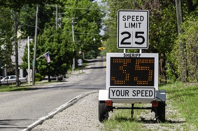 A sign displaying the posted speed limit of 25 mph with a digital sign beneath it displaying 35 mph, indicating the actual speed of the vehicle.